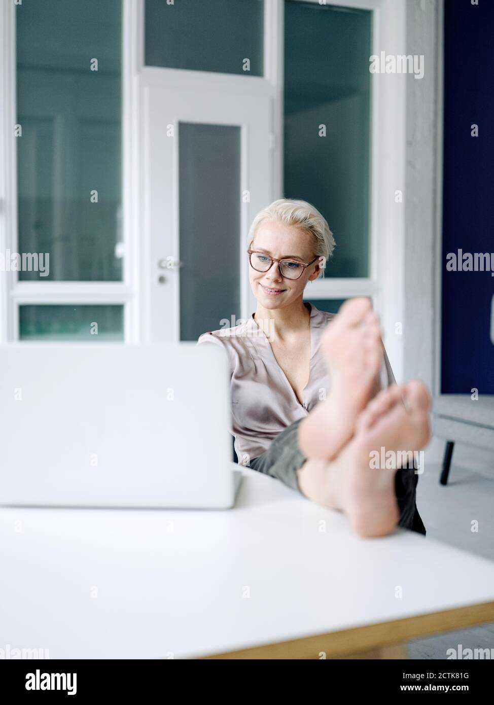 Femme d'affaires avec pieds sur le bureau utilisant un ordinateur portable dans le bureau en mezzanine Banque D'Images