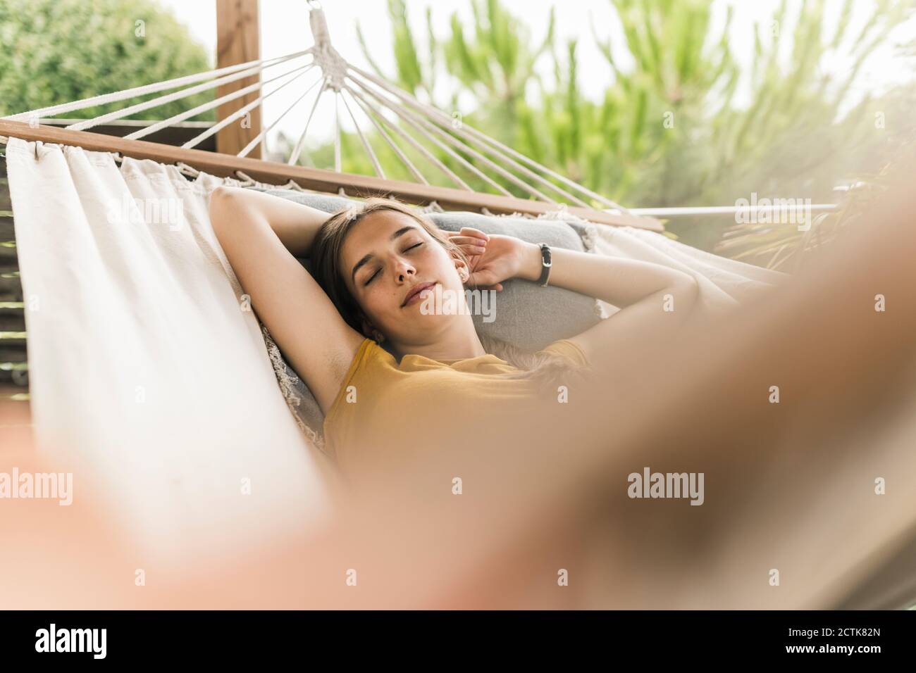 Jeune femme aux bras relevés dormant sur un hamac dans la cour Banque D'Images