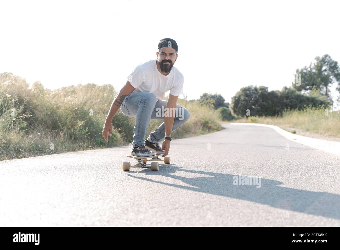 Beau homme skate sur la route contre ciel dégagé Banque D'Images