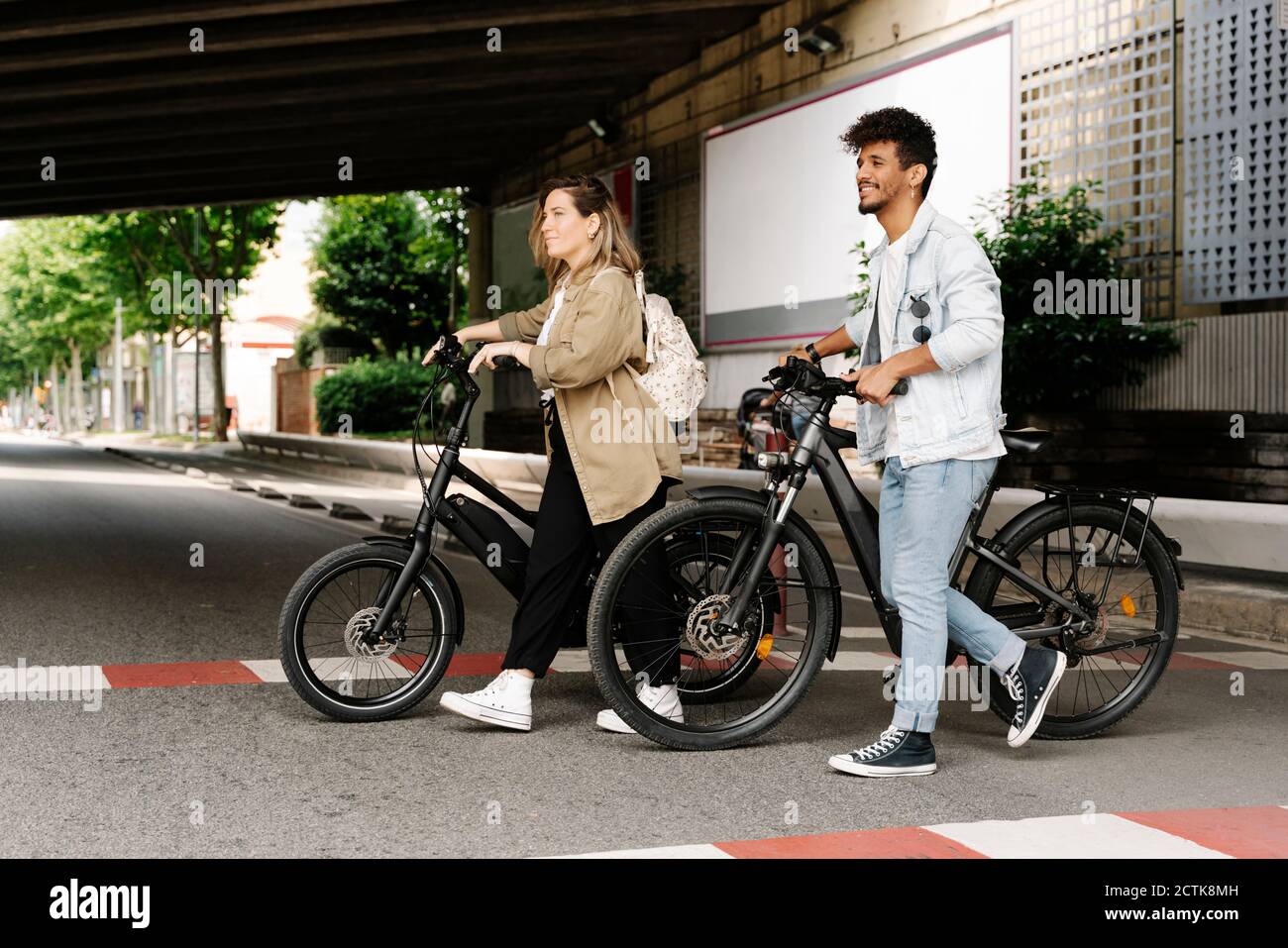 Couple traversant la route avec des vélos électriques dans la ville Banque D'Images