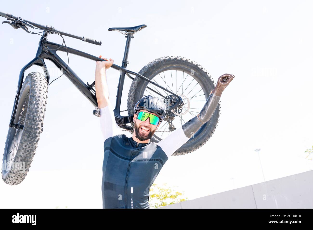 Joyeux athlète masculin en amputation transportant un vélo tout en se tenant contre le clair ciel Banque D'Images