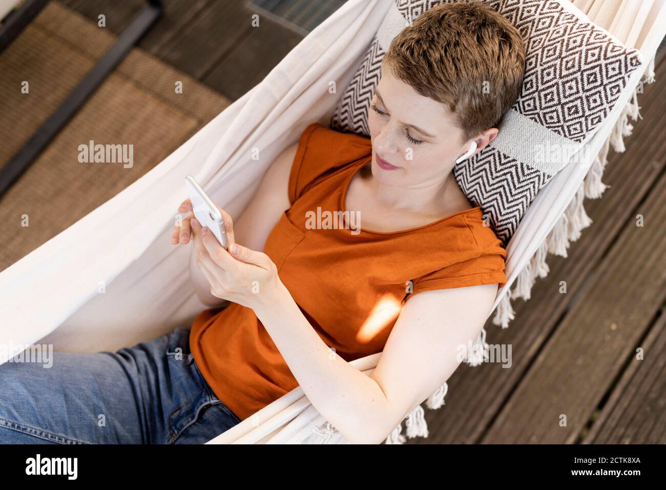 Femme aux cheveux courts utilisant un téléphone portable tout en se relaxant hamac dans le porche Banque D'Images