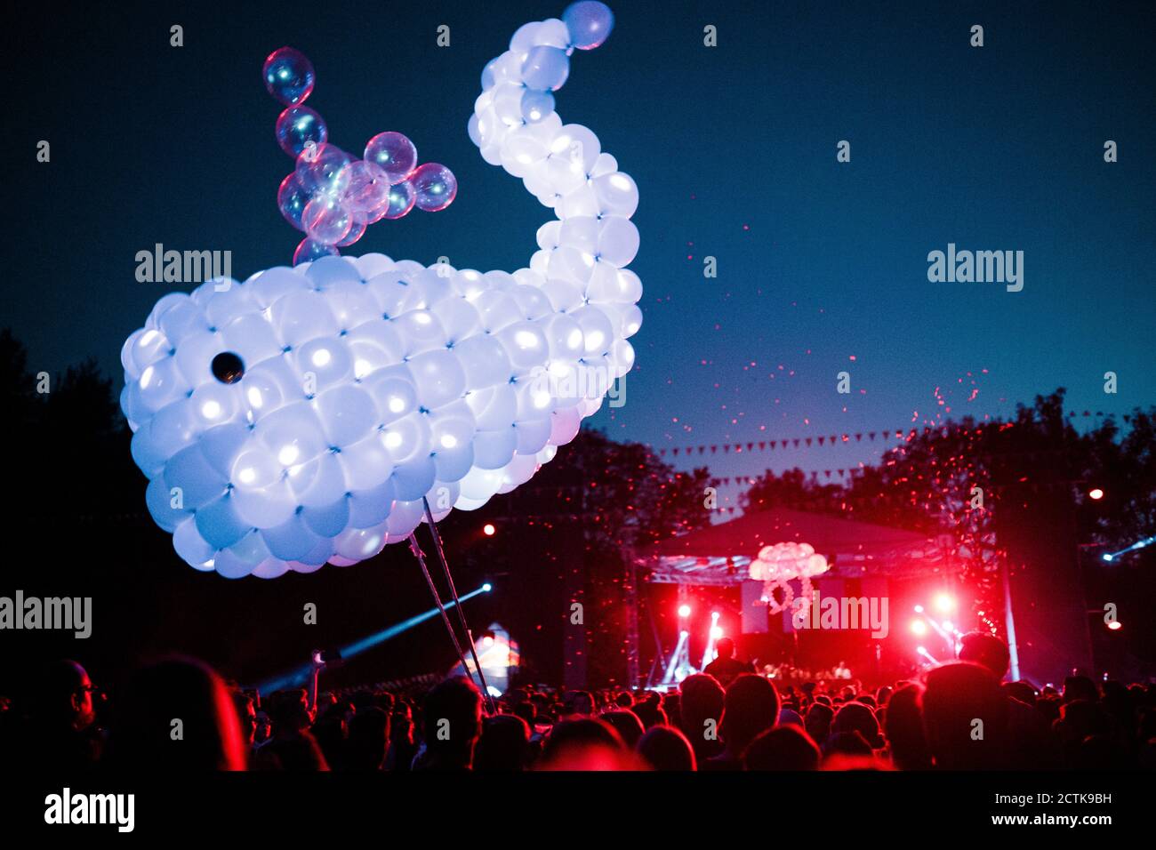 Baleine faite de ballons violets flottant au-dessus de la foule de gens s'amuser pendant le festival de musique de nuit Banque D'Images