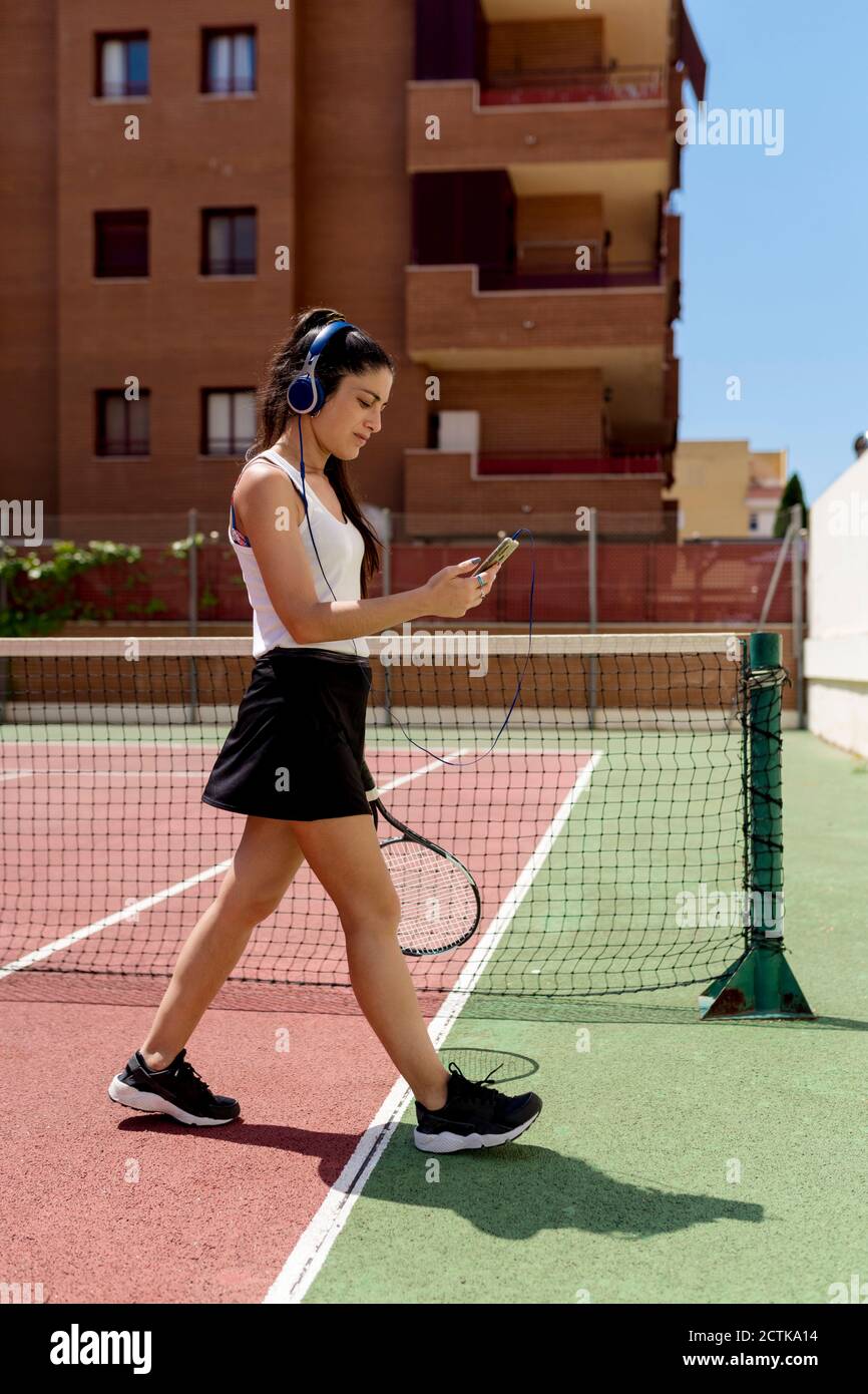 Une femme de tennis porte un casque à l'aide d'un smartphone lorsqu'elle  marche en cour Photo Stock - Alamy