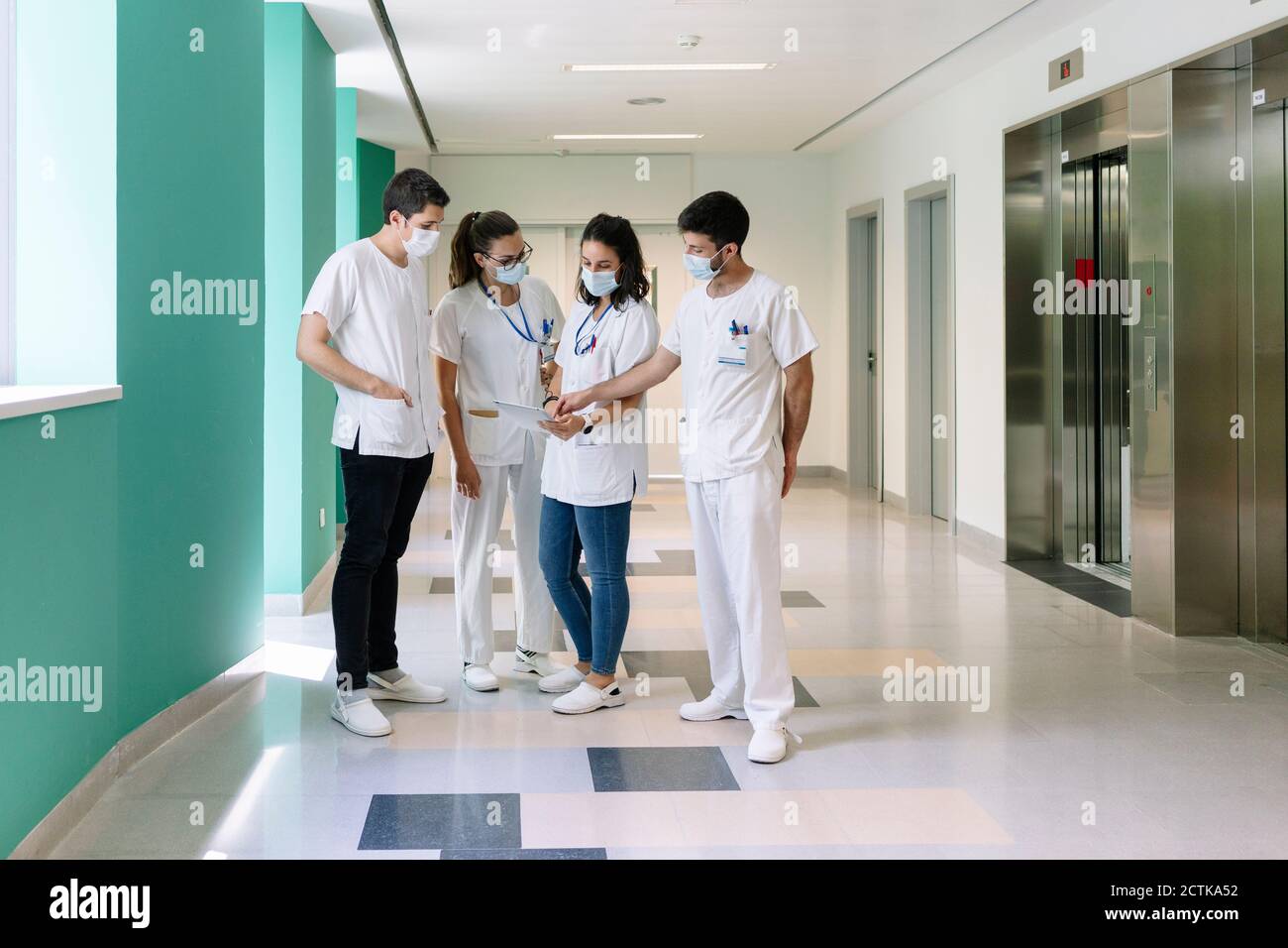 Les médecins portant des masques chirurgicaux discutant au-dessus d'une tablette numérique debout dans un couloir à l'hôpital Banque D'Images