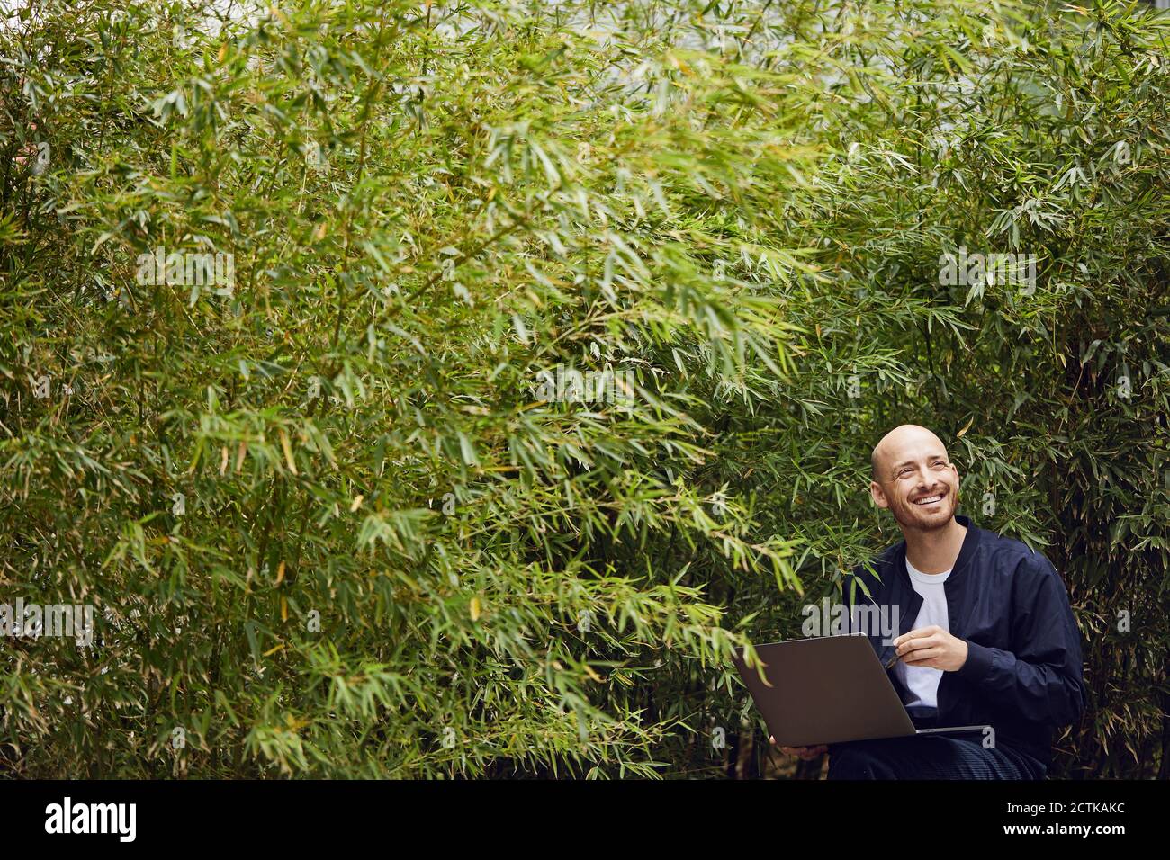 Un homme rit en travaillant sur un ordinateur portable dans un parc public Banque D'Images