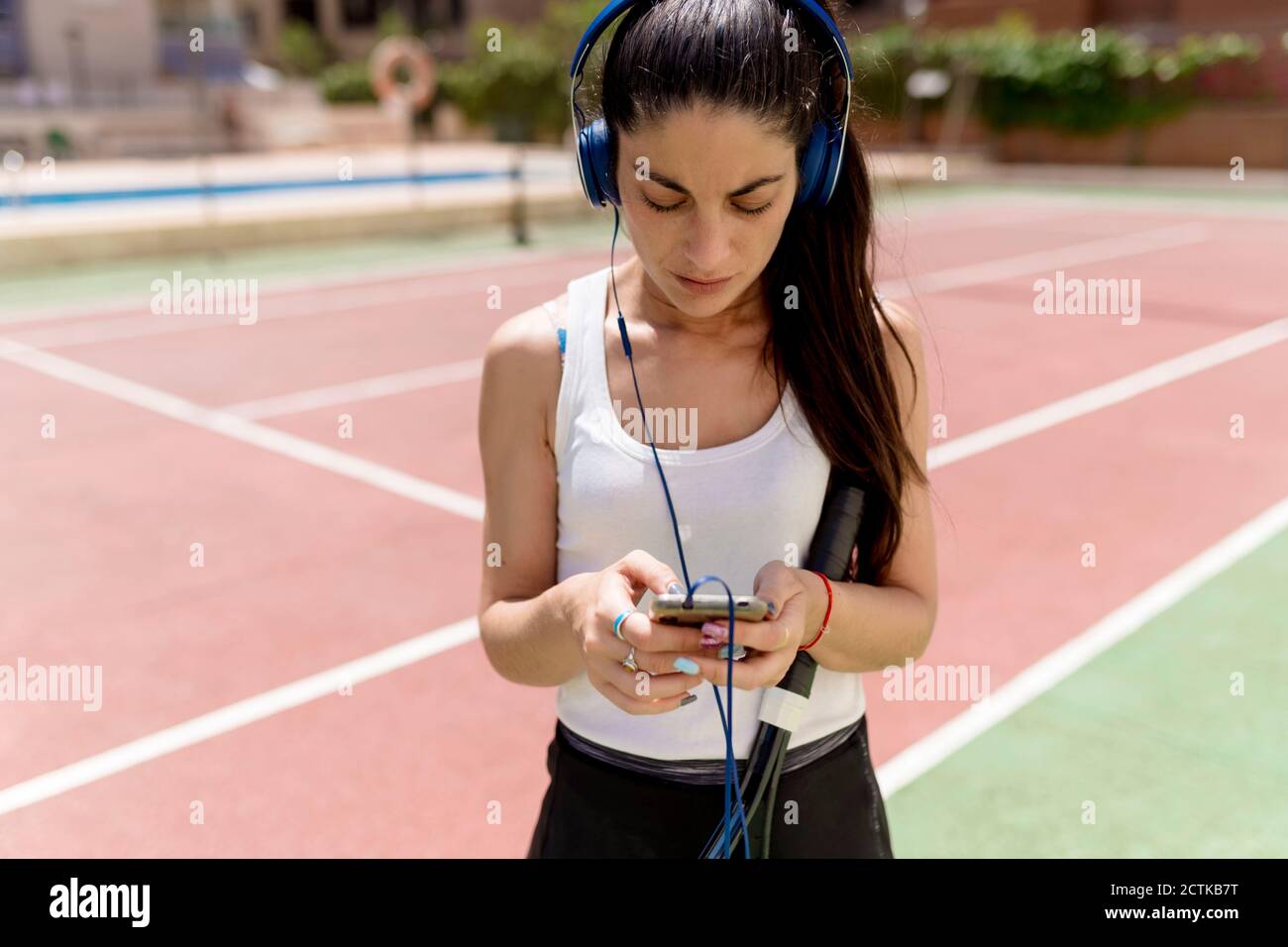 Joueur de tennis féminin utilisant un smartphone tout en écoutant de la musique court le jour ensoleillé Banque D'Images