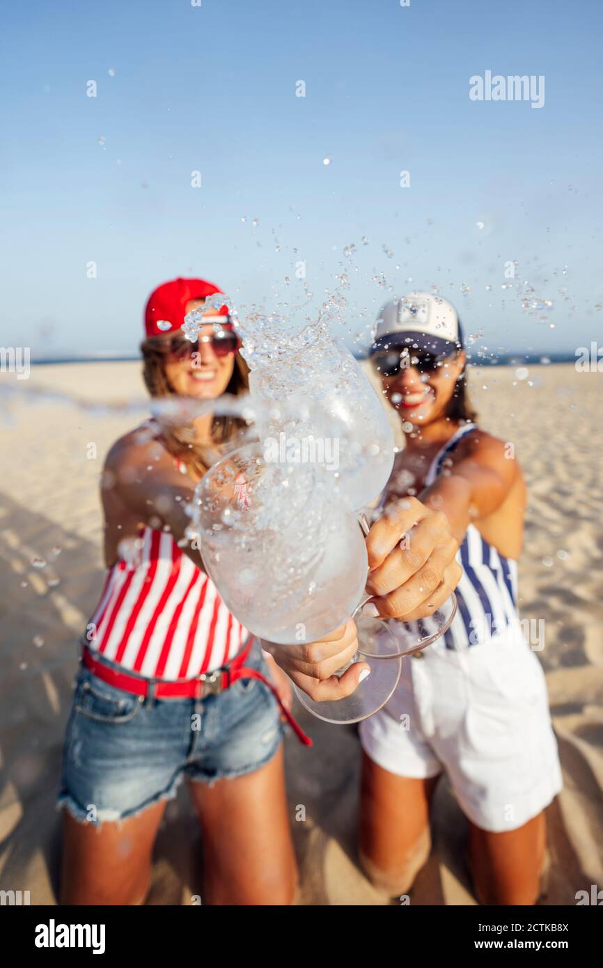 Des amies ludiques barbotent en buvant un verre tout en dorant à la plage jour ensoleillé Banque D'Images