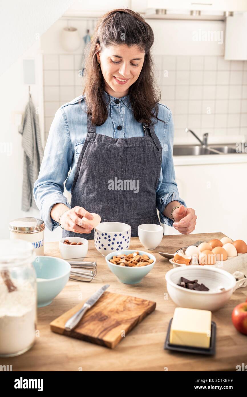 Belle femme cassant l'oeuf en se tenant à l'île de cuisine Banque D'Images