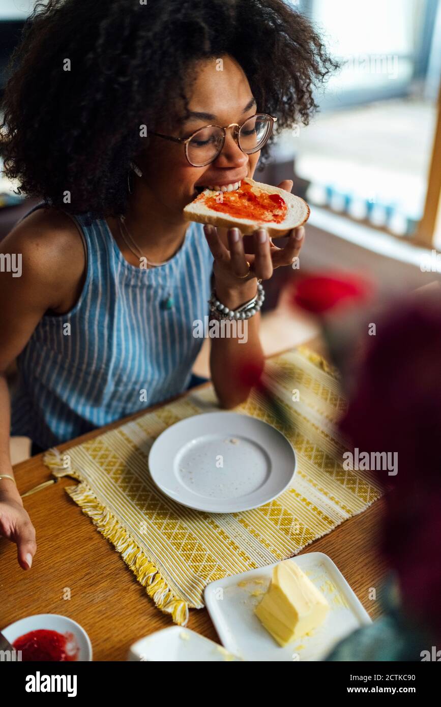 Jeune femme avec les yeux fermés manger du pain tout en s'asseyant à tableau Banque D'Images