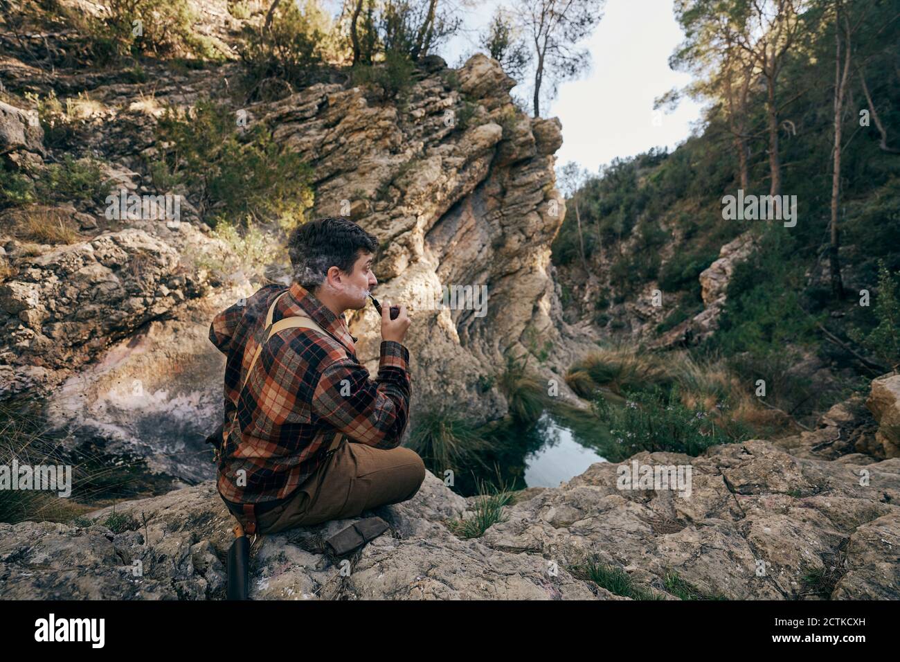 Bushcrafter fumant pipe tout en étant assis sur la formation de roche Banque D'Images