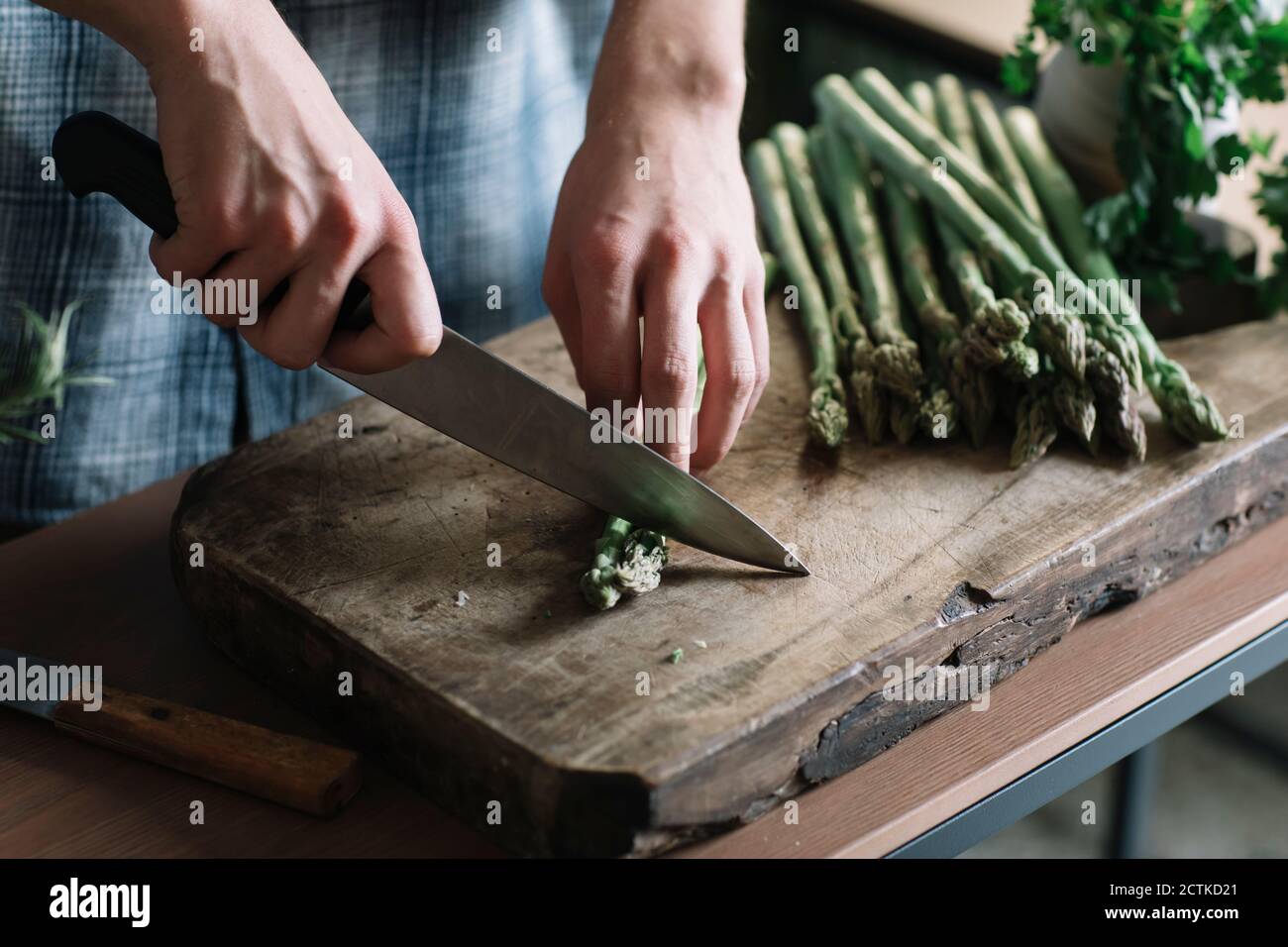 Mains de l'homme coupant des asperges fraîches à bord dans la cuisine Banque D'Images