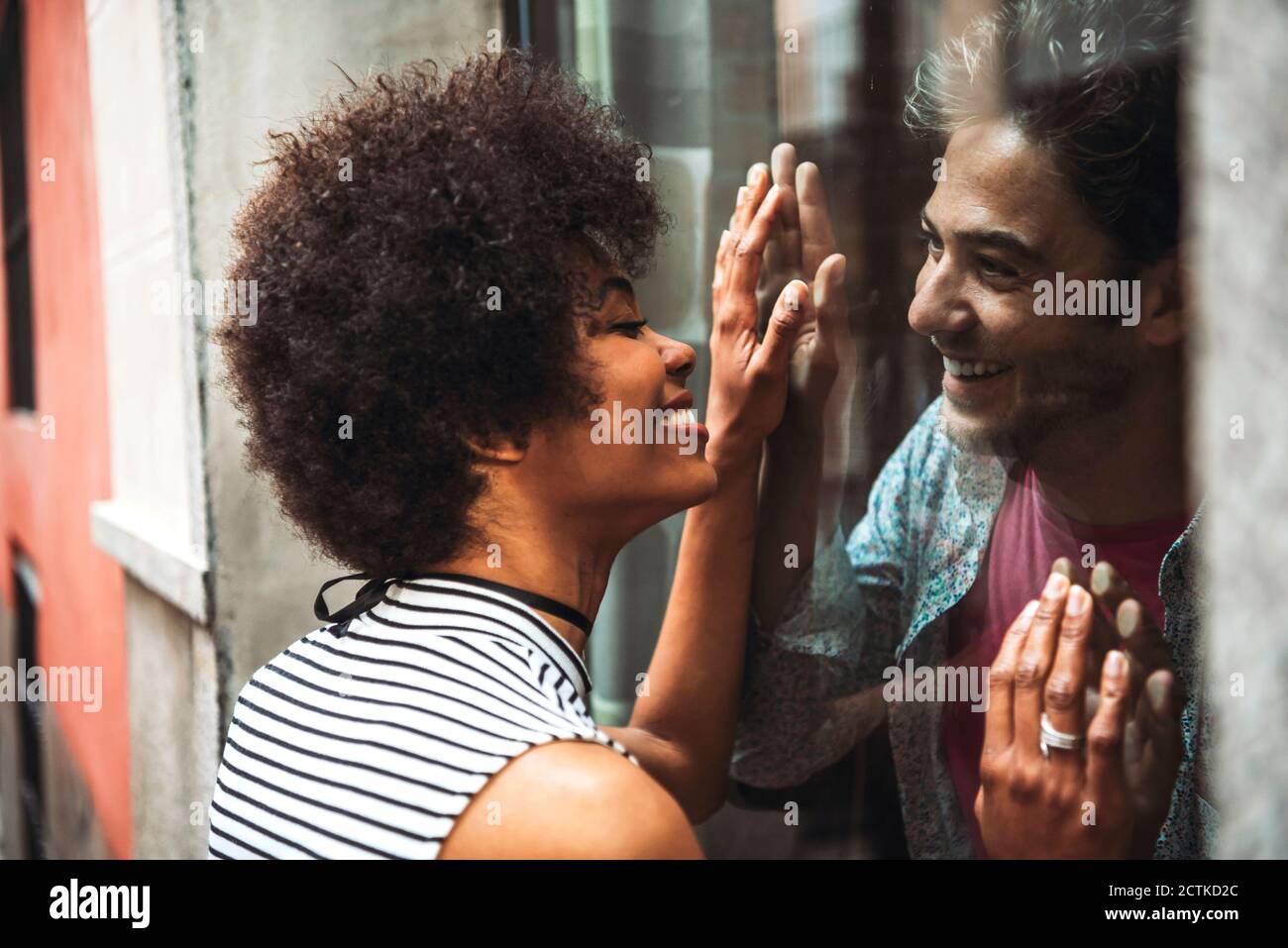 Gros plan d'une femme souriante avec des cheveux bouclés regardant un petit ami par la fenêtre du café Banque D'Images