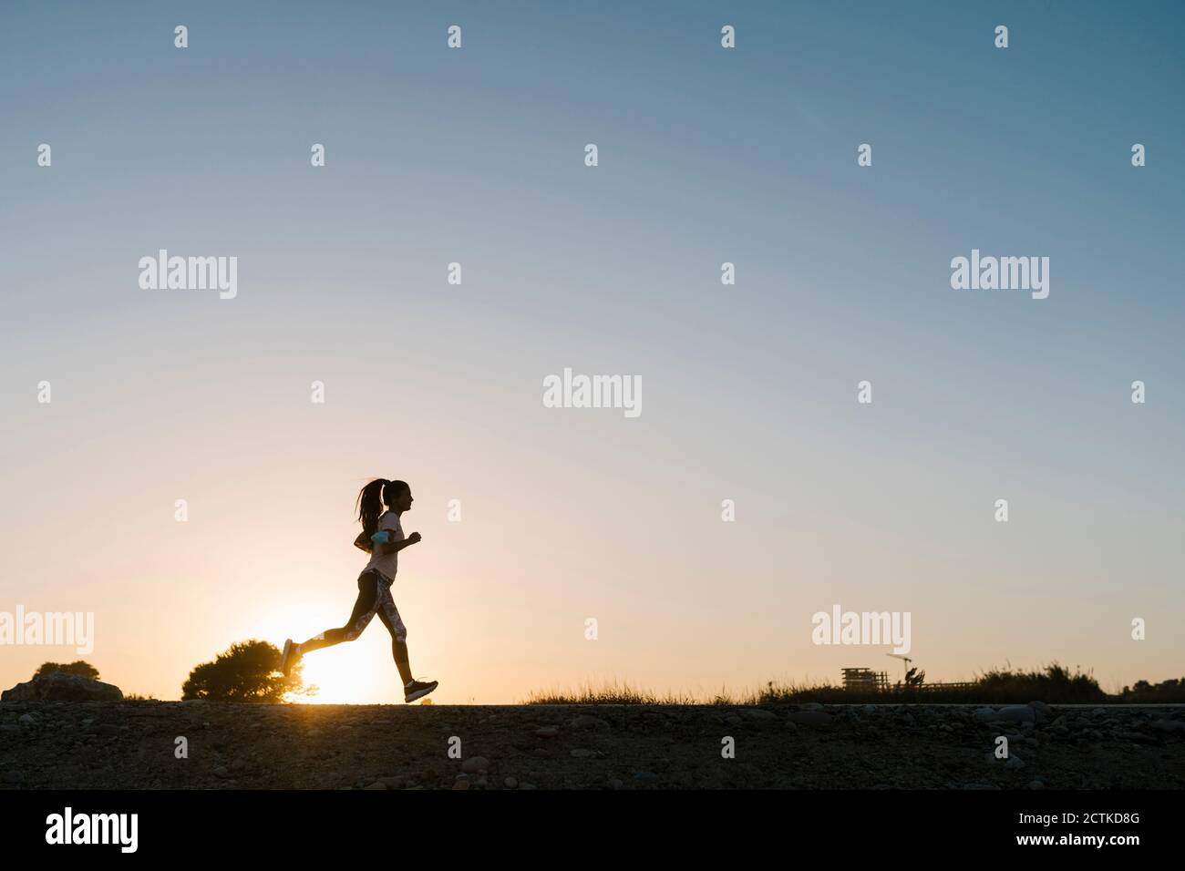 Silhouette d'une femme qui court dans un ciel dégagé au coucher du soleil Banque D'Images