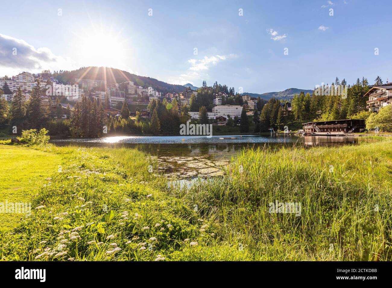 Suisse, canton des Grisons, Arosa, Soleil brillant sur la rive du lac Untersee en été avec ville en arrière-plan Banque D'Images