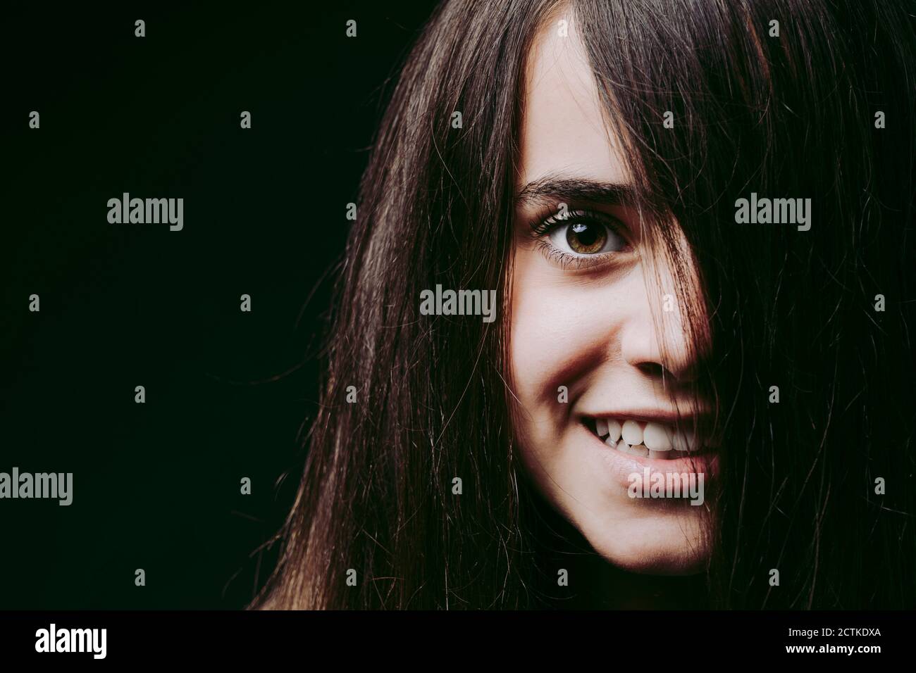Gros plan d'une fille souriante avec des cheveux bruns sur le visage contre arrière-plan noir Banque D'Images