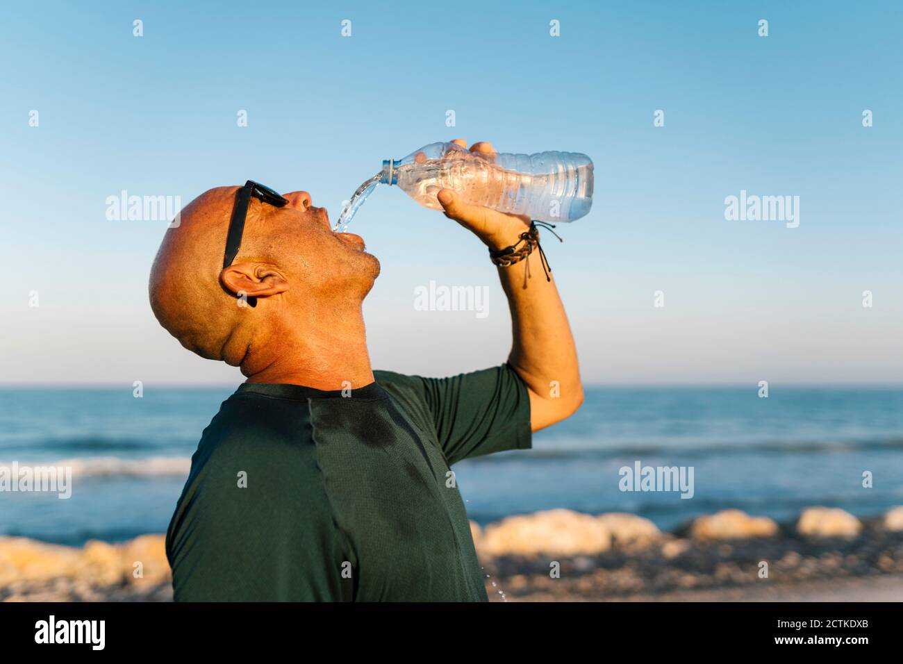 Homme senior buvant de l'eau en se tenant contre le ciel clair Banque D'Images