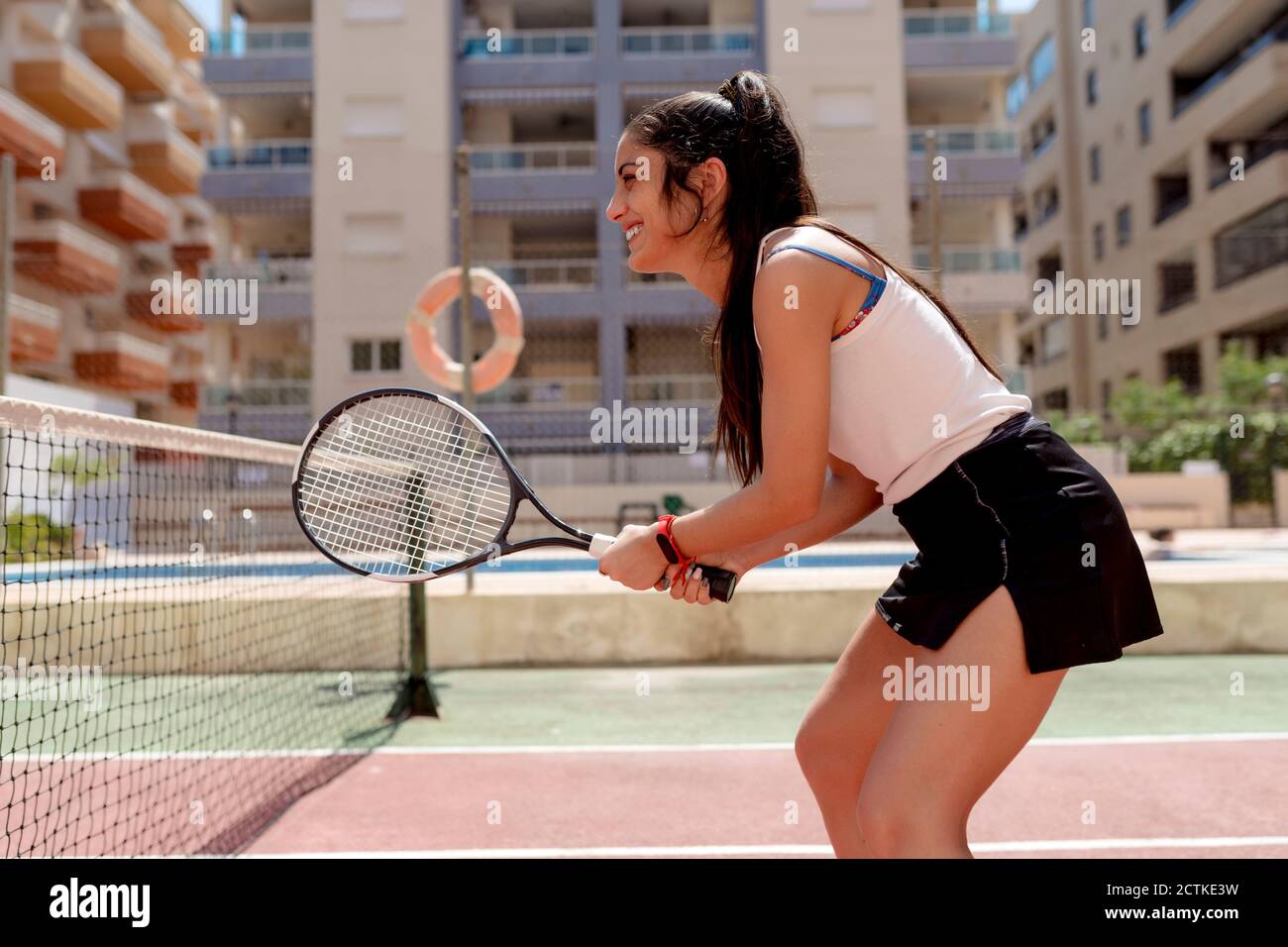 Femme jouant au tennis contre des bâtiments dans le court le jour ensoleillé Banque D'Images