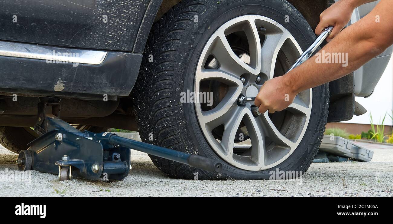 Homme changer de roue. Changer de pneu changer de pneu de voiture à plat.  Aide sur le concept de route. Les mains du mécanicien dévisse un pneu crevé  d'une voiture soulevée sur