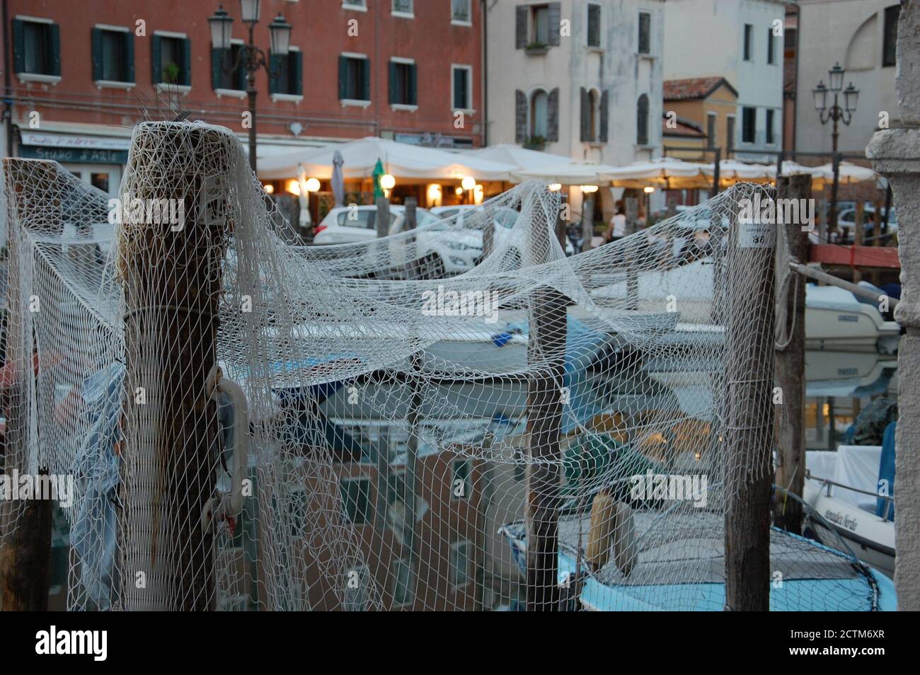 un filet de poisson séchant sur quelques poteaux en bois dans un canal de Chioggia dans la lagune vénitienne avec des bateaux et des lumières de rue en arrière-plan Banque D'Images