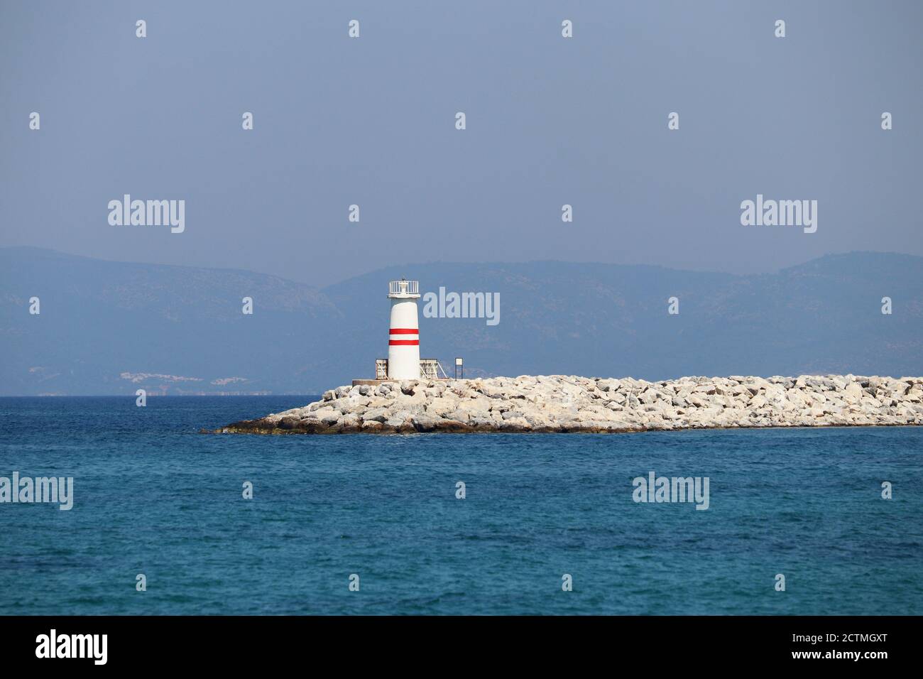 Tour de phare sur un quai en pierre dans la mer d'azur contre montagnes brumeuses Banque D'Images