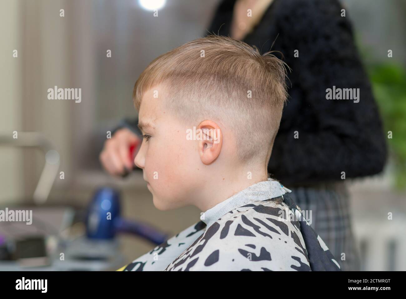 Vue latérale Happy boy est assis dans le salon de coiffure avec des cheveux mouillés et lui coupe les cheveux. Banque D'Images