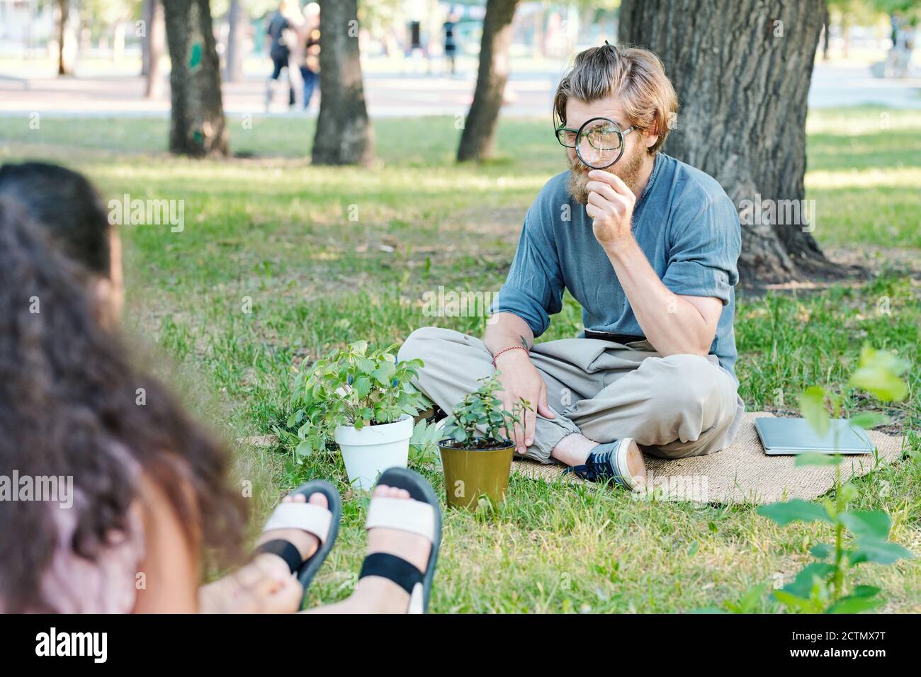Professeur barbu en lunettes de vue en utilisant la loupe tout en faisant la recherche avec des élèves en classe en plein air Banque D'Images