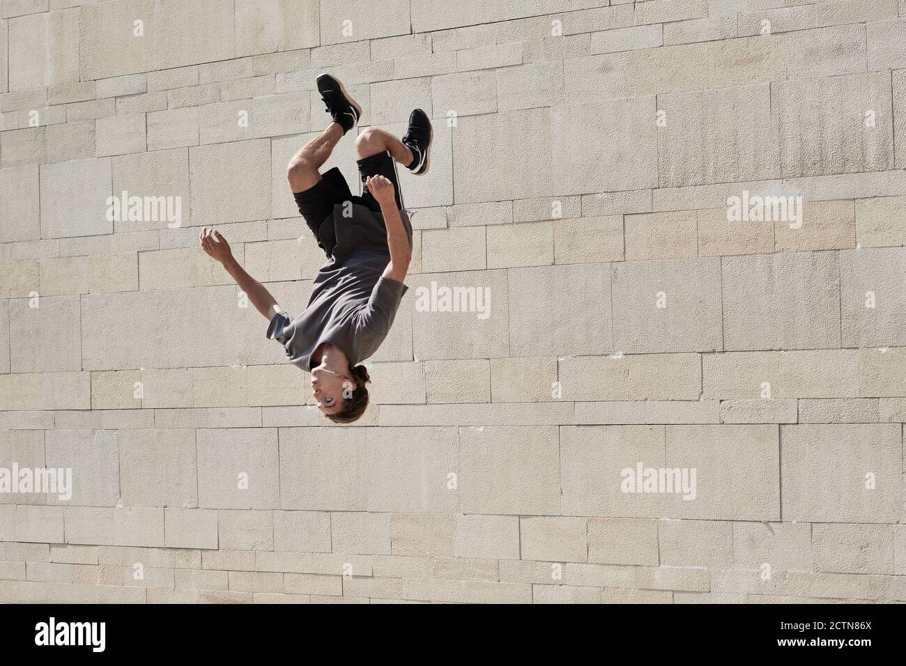 À l'envers de jeunes hommes faisant du somersault en pratiquant le parkour en zone urbaine en été Banque D'Images