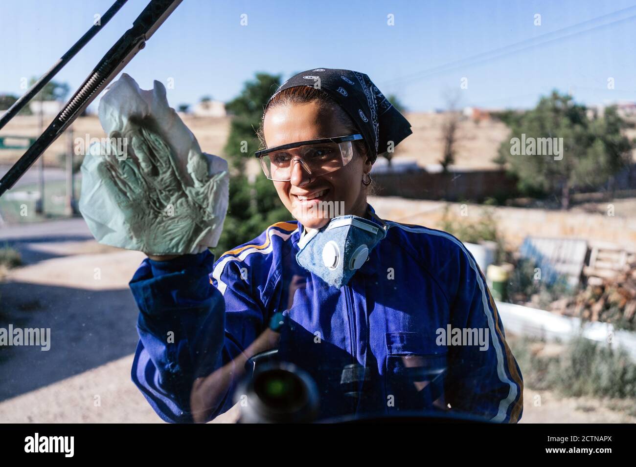 Femme souriante travaillant en uniforme et lunettes de protection pour nettoyer la fenêtre de la machine dans la zone industrielle Banque D'Images