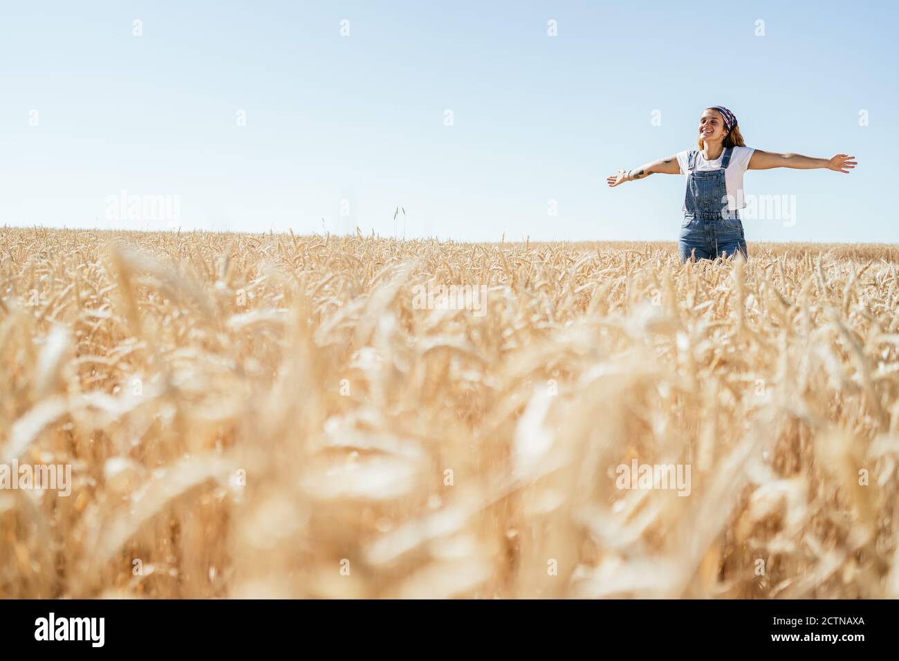 Une femme ravie dans une combinaison en denim avec un champ de blé bras étirés et nature Banque D'Images