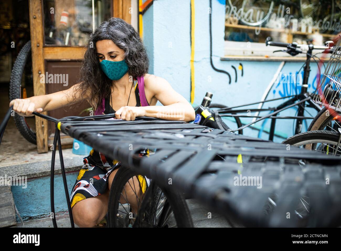 Femme sérieuse ethnique technicien dans le masque de protection travaillant avec le pneu sangles pour vélos près de l'entrée de l'atelier Banque D'Images