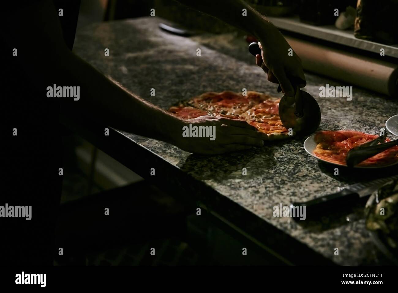 Croiser la pizza anonyme en coupant des pizzas chaudes fraîchement préparées sur un comptoir en marbre tout en travaillant dans la cuisine du restaurant Banque D'Images