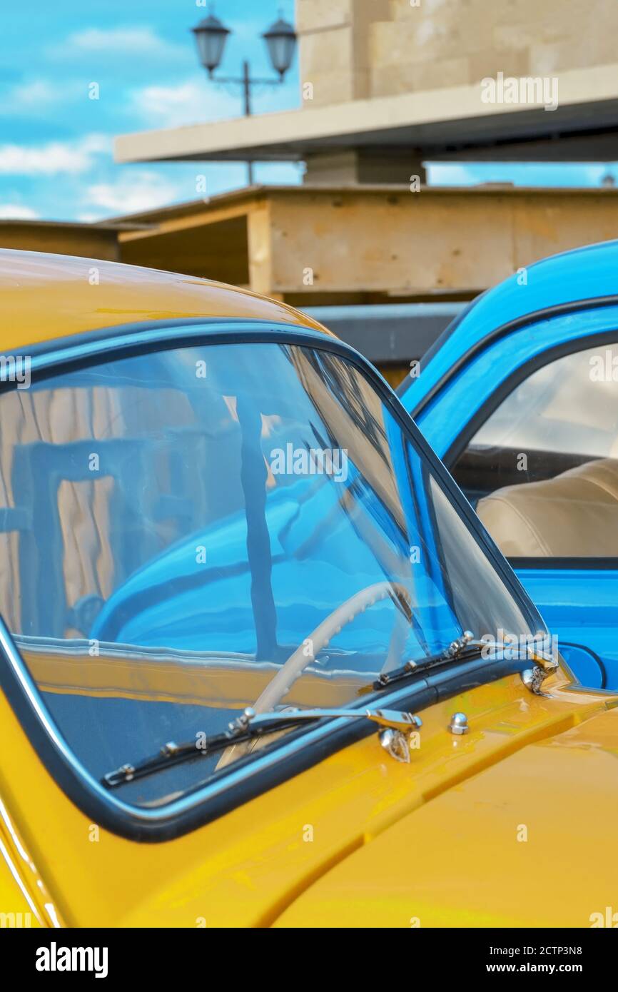 Capot et pare-brise d'une voiture jaune sur le fond d'un gros plan de voiture bleue. Banque D'Images