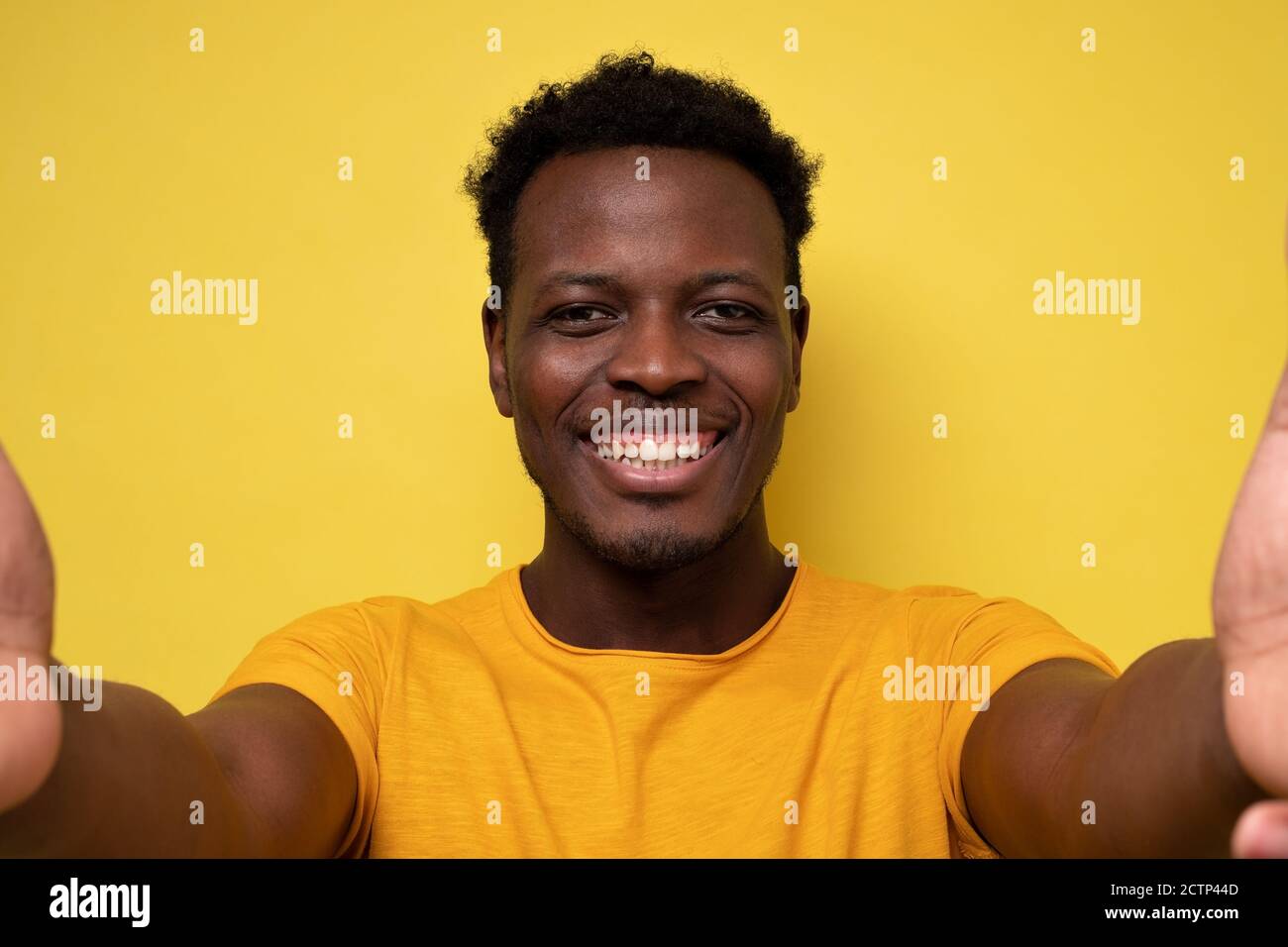 Souriant jeune homme africain faisant le selfie sur fond jaune Banque D'Images