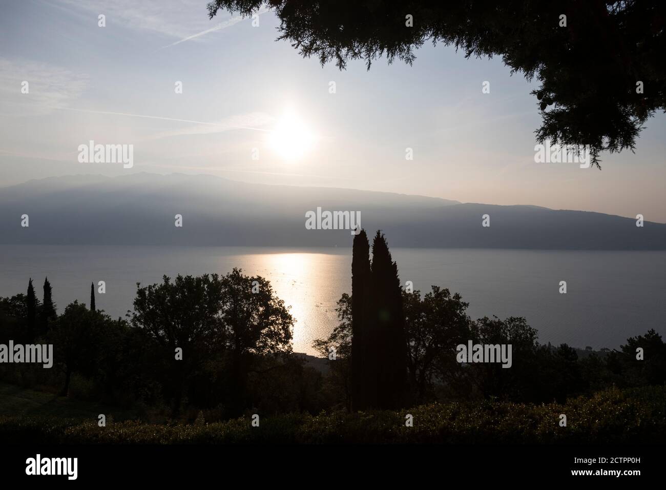 Le soleil commence à brûler tôt le matin brouillard sur les montagnes comme il brille sur la surface du lac de Garde (Lago di Garda) au-dessus de Gargagno, Italie. Banque D'Images