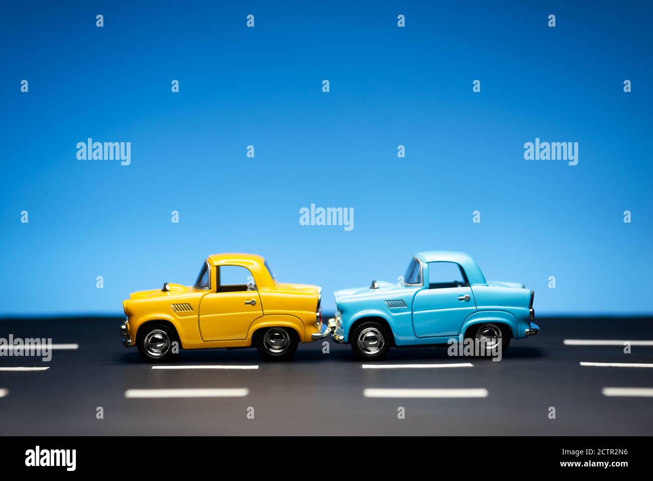 Deux vieux modèles de voitures des années 50, un jaune et un bleu, se tiennent sur une route et sur un fond bleu. Banque D'Images