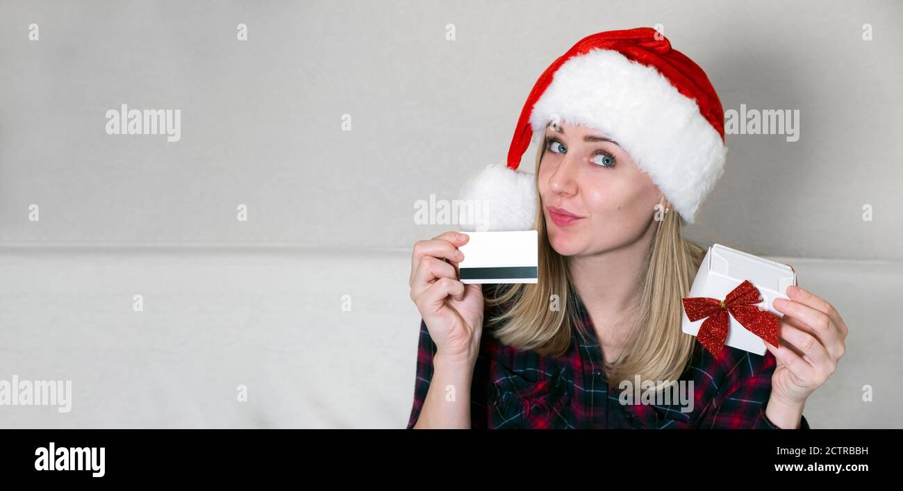 Shopping de Noël à la maison. Femme rêveuse tenant une carte et une boîte cadeau. Femme portant un chapeau de noël rouge, se préparant à Noël. Ventes de vacances d'hiver Banque D'Images