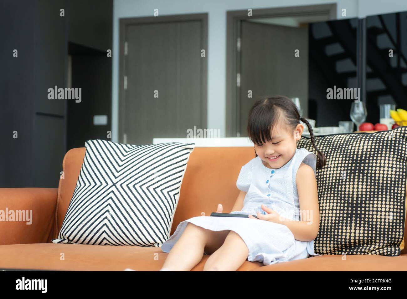 Enfant asiatique mignon à l'aide d'un smartphone et souriant pour regarder vidéo ou jeu en étant assis sur un canapé dans la salle de séjour chambre à la maison Banque D'Images