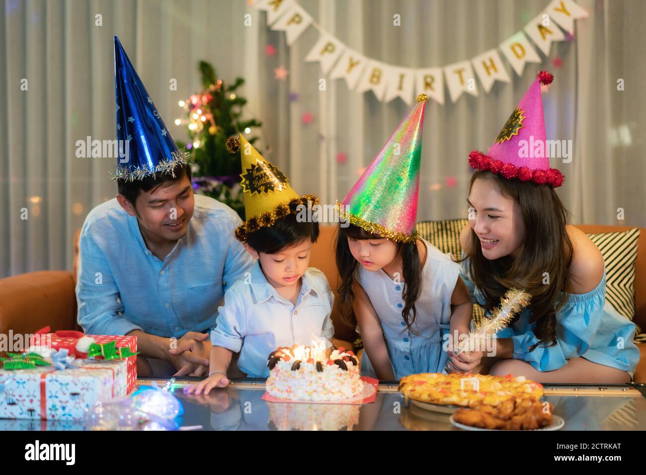 Famille heureuse asiatique dans une fête d'anniversaire pour sa fille et son fils alors que la fille est sur le point de souffler les bougies la nuit dans le salon à la maison. Banque D'Images