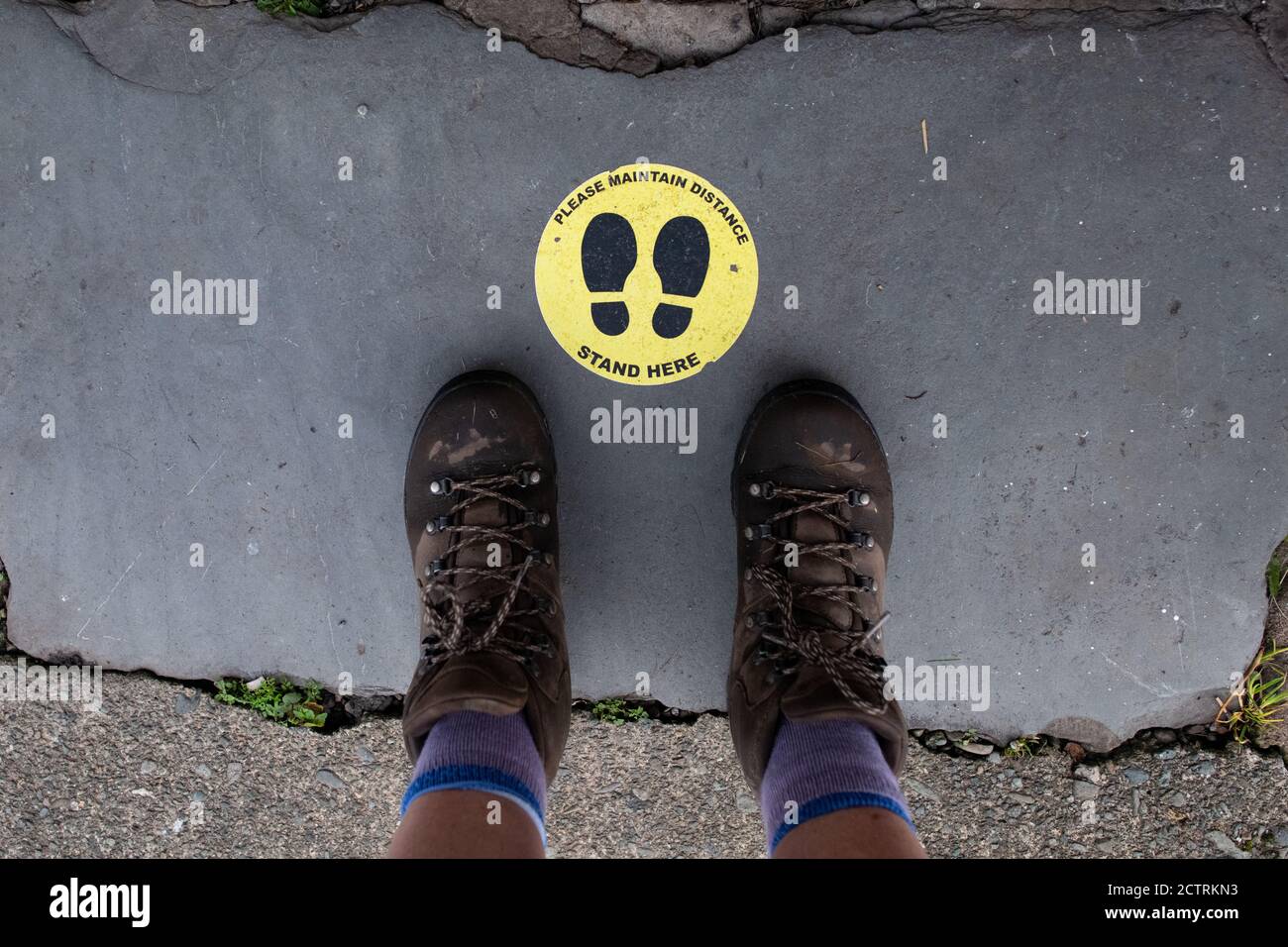 Walker portant des bottes de marche debout à côté d'un panneau social de distanciation à l'entrée du pub pendant la pandémie du coronavirus dans le Lake District, Angleterre, Royaume-Uni Banque D'Images