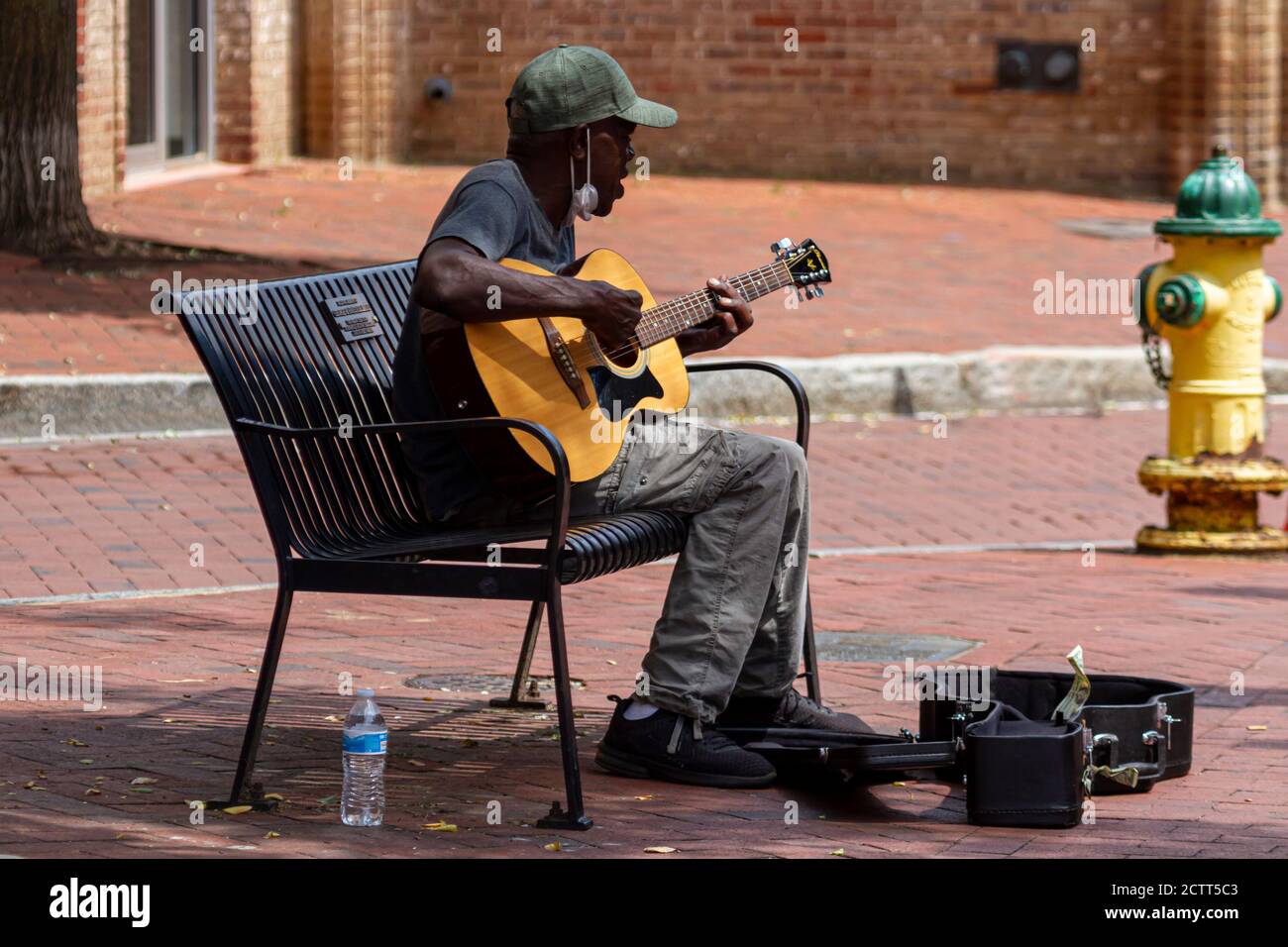 Annapolis, MD 08/21/2020: Un homme afro-américain âgé portant un chapeau de baseball et un masque de visage joue de la guitare classique et chante en étant assis o Banque D'Images
