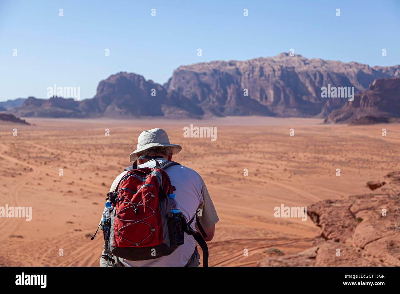 Un touriste d'âge moyen occidental portant un sac à dos rouge et chapeau solaire est debout sur le bord d'un grès falaise donnant sur les vastes terres désertiques Banque D'Images