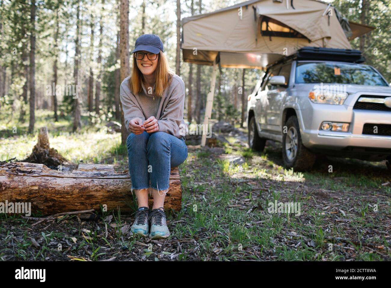 Portrait d'une femme souriante assise en rondins sur le camping, voiture avec tente en arrière-plan, Wasatch cache National Forest Banque D'Images