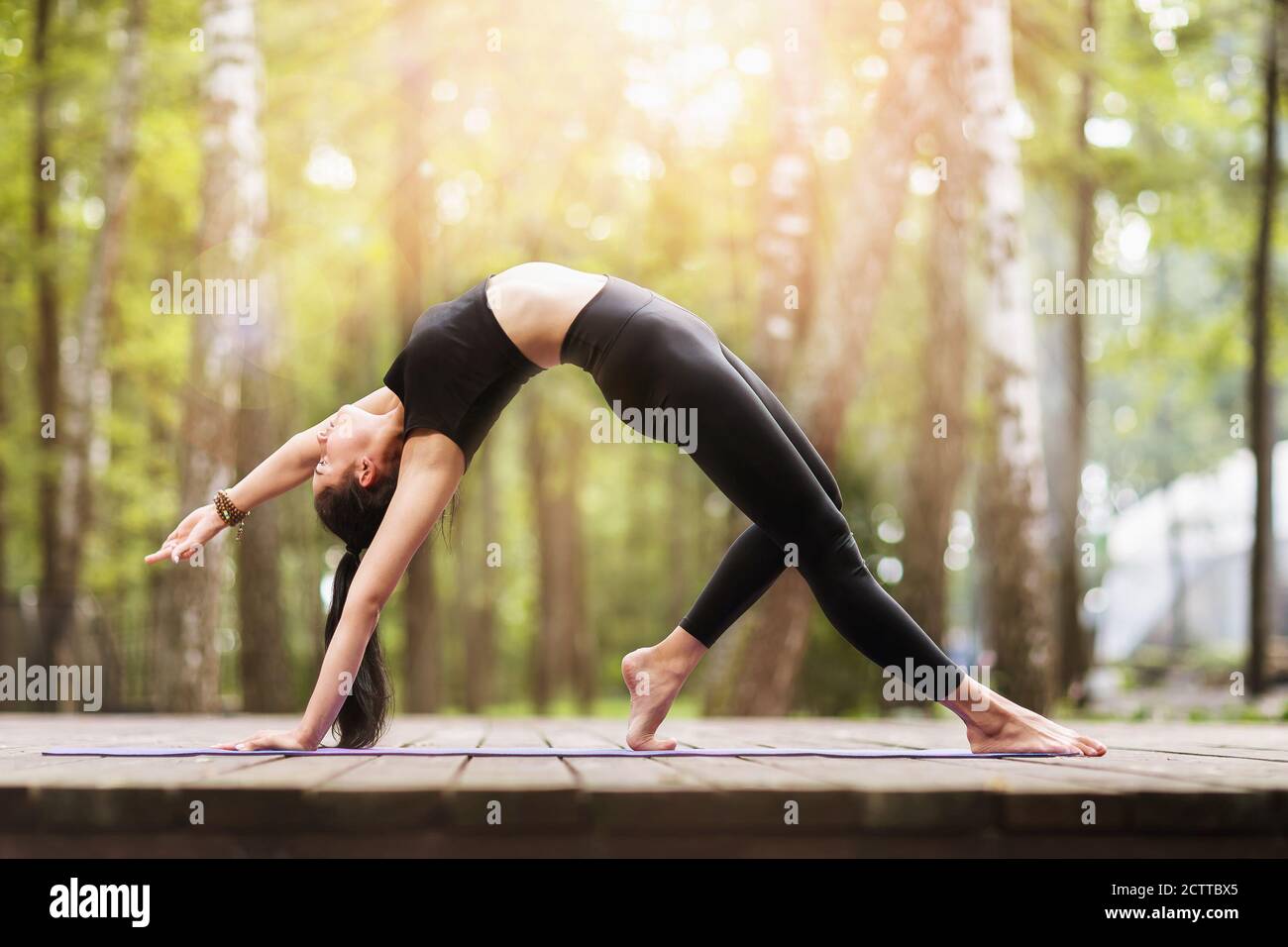 Jeune femme en noir sportswear exécute l'exercice de pont dans le parc, Camatkarasana asana, dancing chien yoga pose Banque D'Images