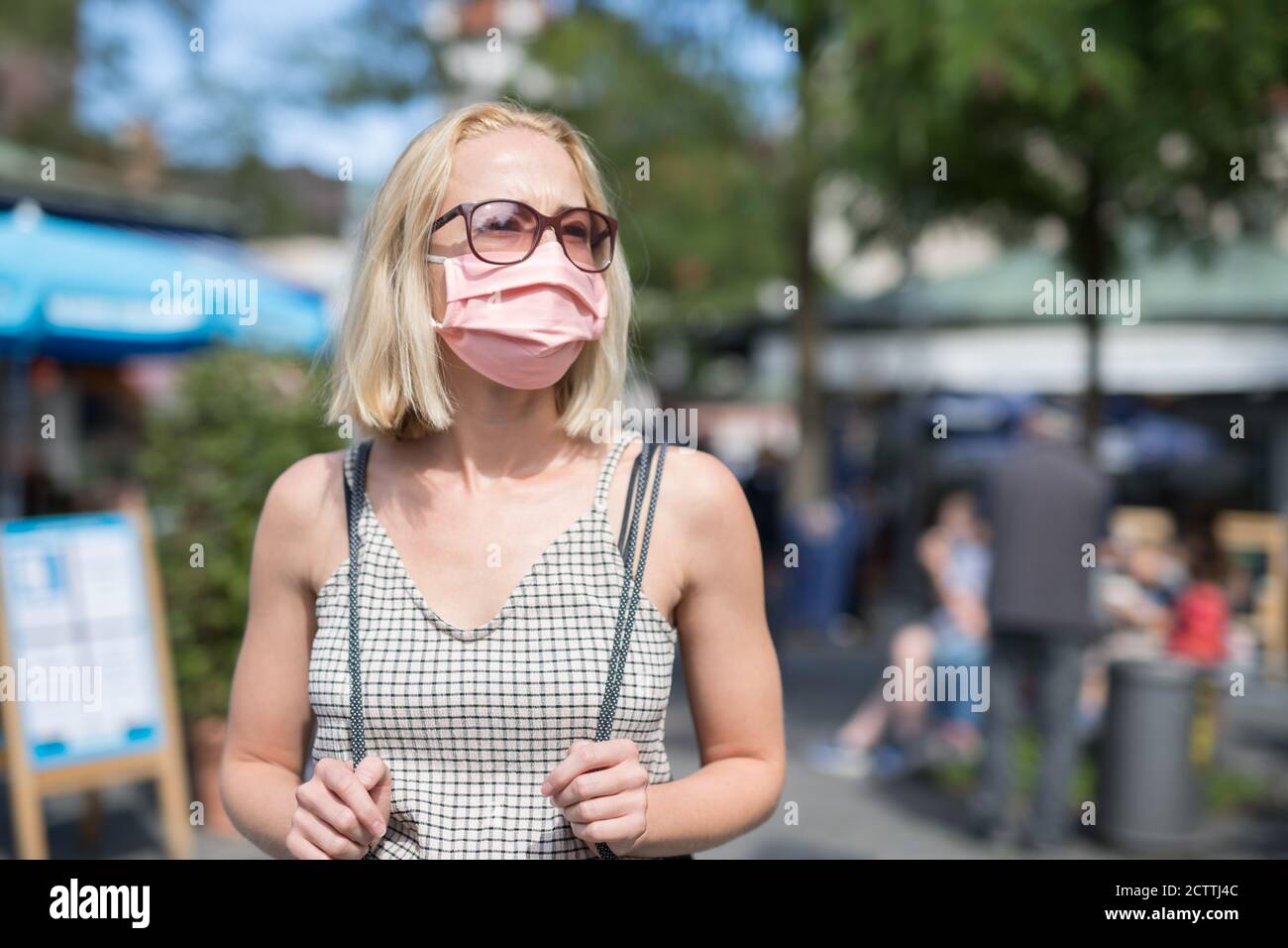 Portrait d'une jeune femme qui marche dans la rue et qui porte un masque de protection contre le virus Covid-19. Personnes fortuites en arrière-plan Banque D'Images