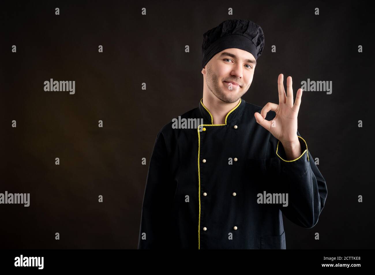 Portrait d'un jeune homme vêtu d'un costume de chef noir Affichage du signe OK posé sur un fond marron avec copie espace publicitaire Banque D'Images