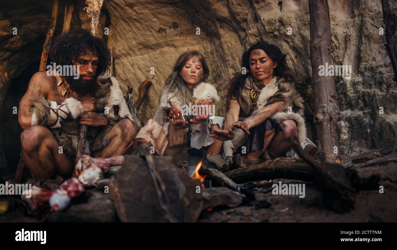 La tribu des chasseurs-cueilleurs préhistoriques portant des peaux d'animaux vit dans une grotte la nuit. Neanderthal ou Homo Sapiens famille essayant de se réchauffer à la Banque D'Images