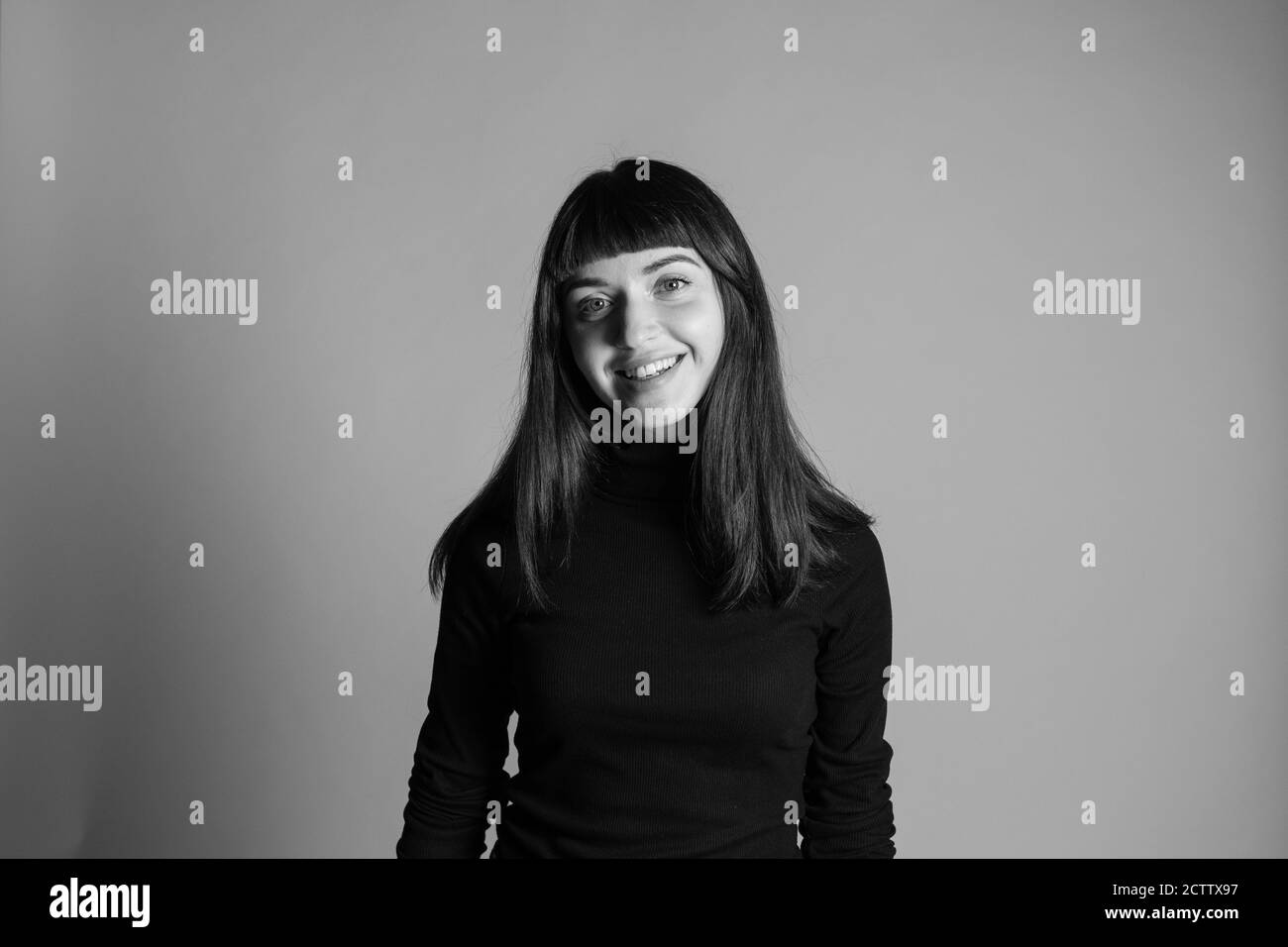Portrait studio d'une jolie femme brune, portant un pull à col roulé noir plié, regardant l'appareil photo, sur un fond gris Uni Banque D'Images
