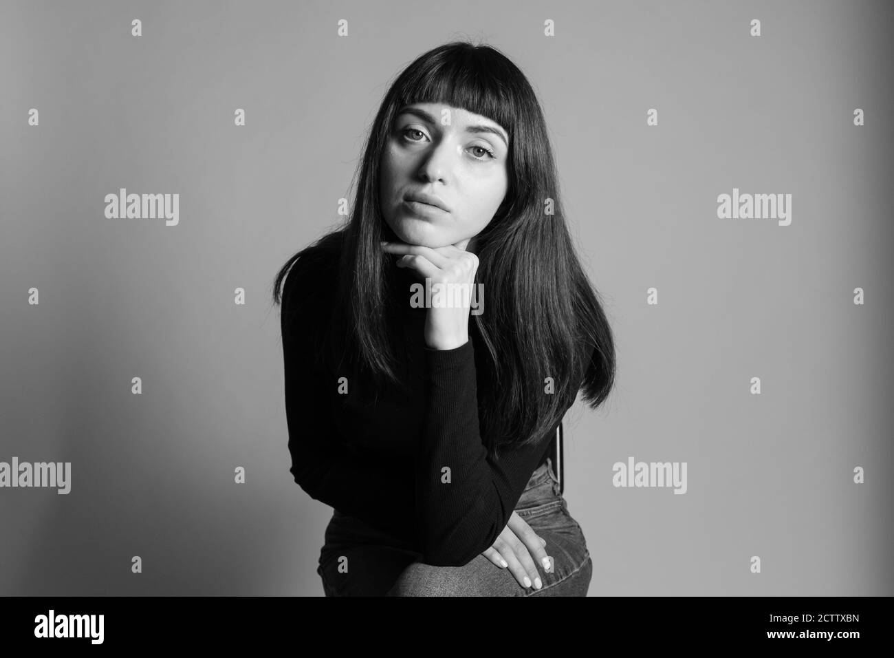 Portrait studio d'une jolie femme brune, portant un pull à col roulé noir plié, regardant l'appareil photo, sur un fond gris Uni Banque D'Images