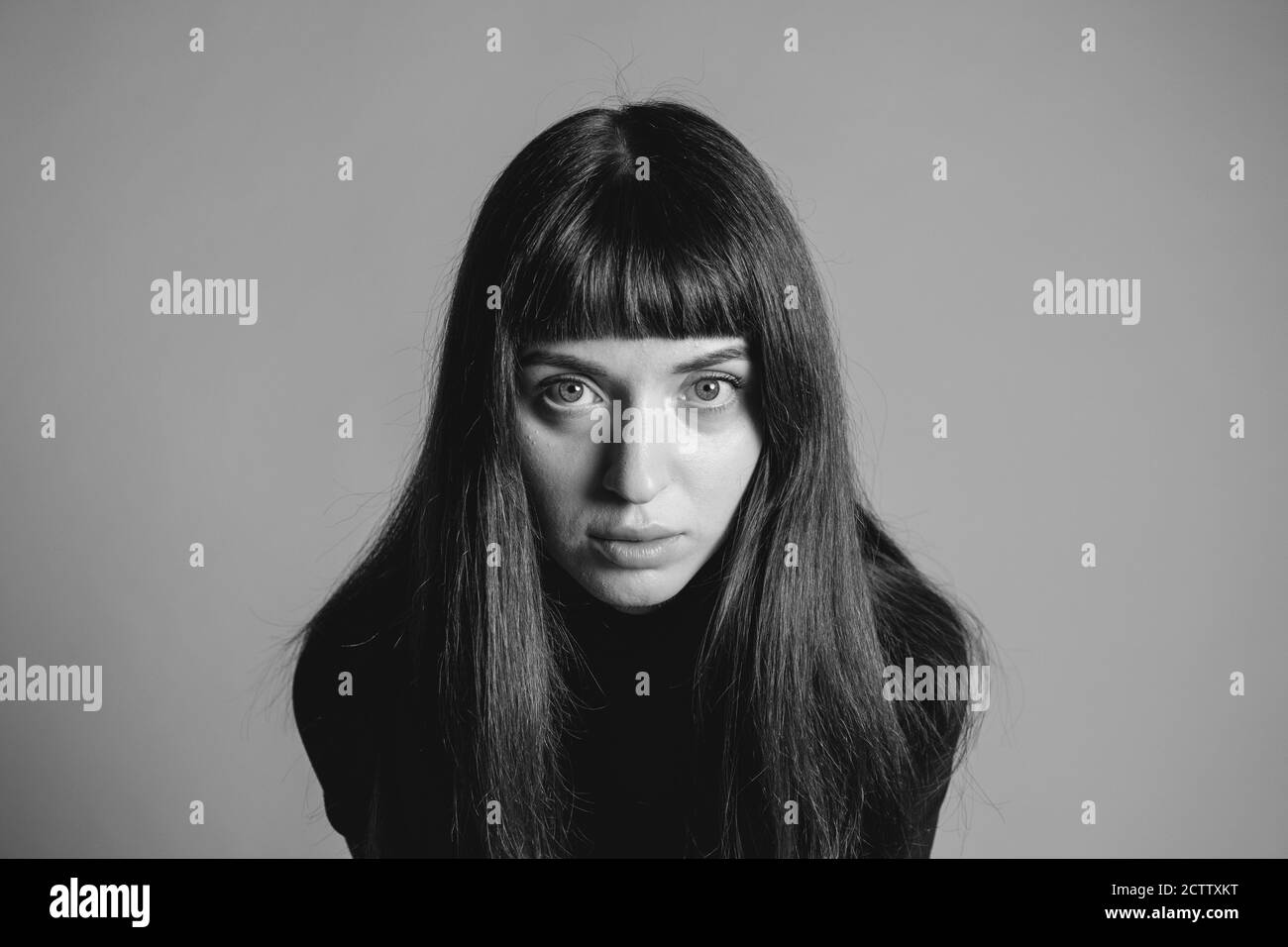 Gros plan portrait en studio d'une jolie femme brunette, regardant l'appareil photo, sur un fond gris Uni Banque D'Images